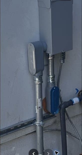 Exterior electrical service panel and conduit on a stucco wall.